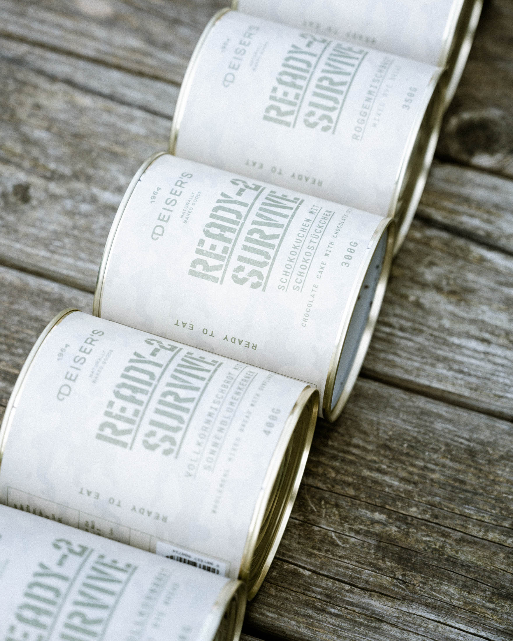 Auf einem Holzboden liegen fünf Dosen von der Serie Deiser's Ready-2-Survive.