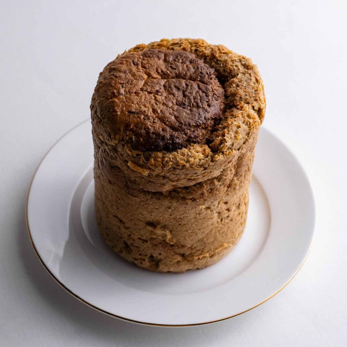 Das Hanfbrot aus der Dose genommen von Deiser's naturally baked goods im Ganzen, auf einem weißen Teller mit goldenem Rand.