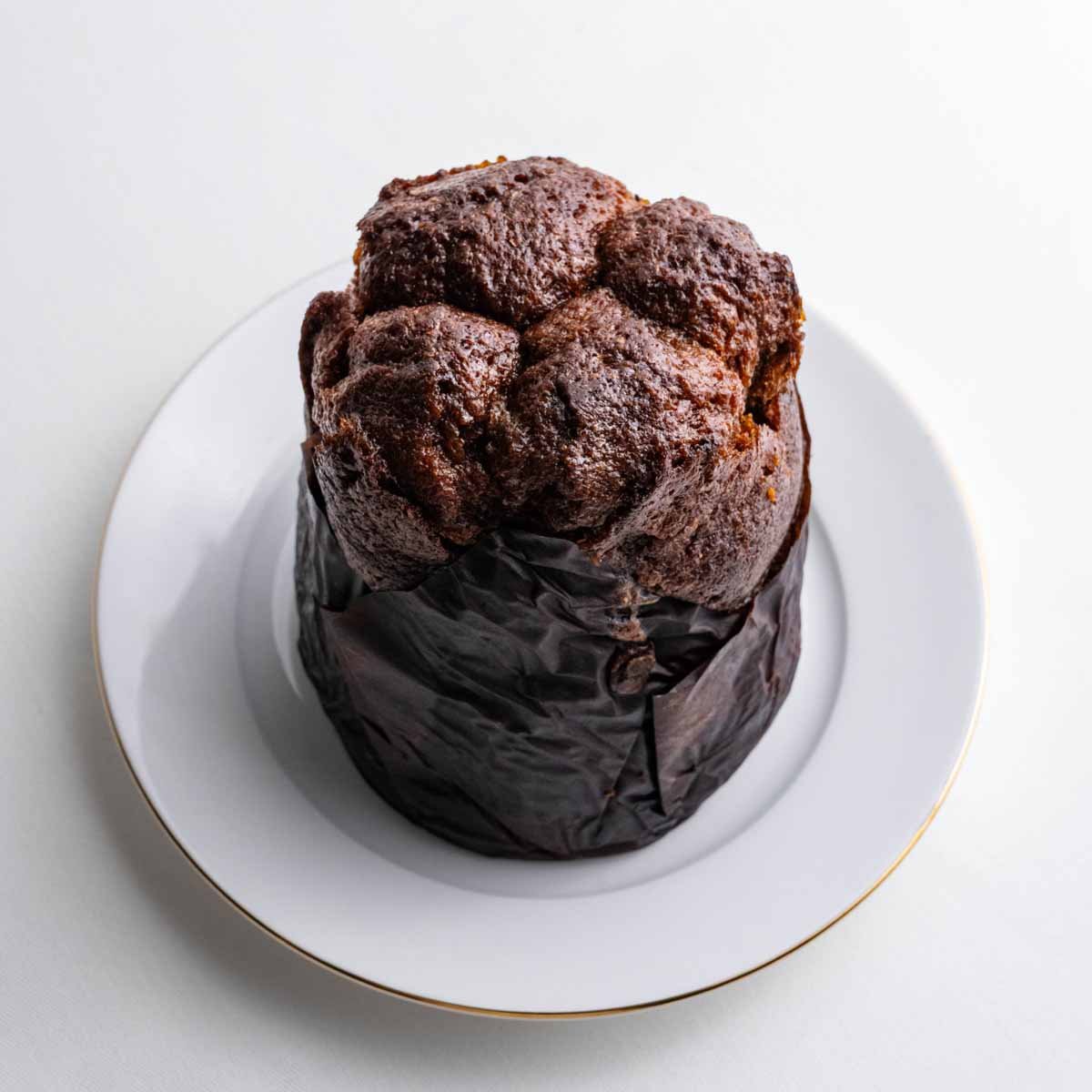 Der Schokokuchen aus der Dose genommen von Deiser's naturally baked goods im Ganzen, unten umhüllt mit Backpapier, auf einem weißen Teller mit goldenem Rand.