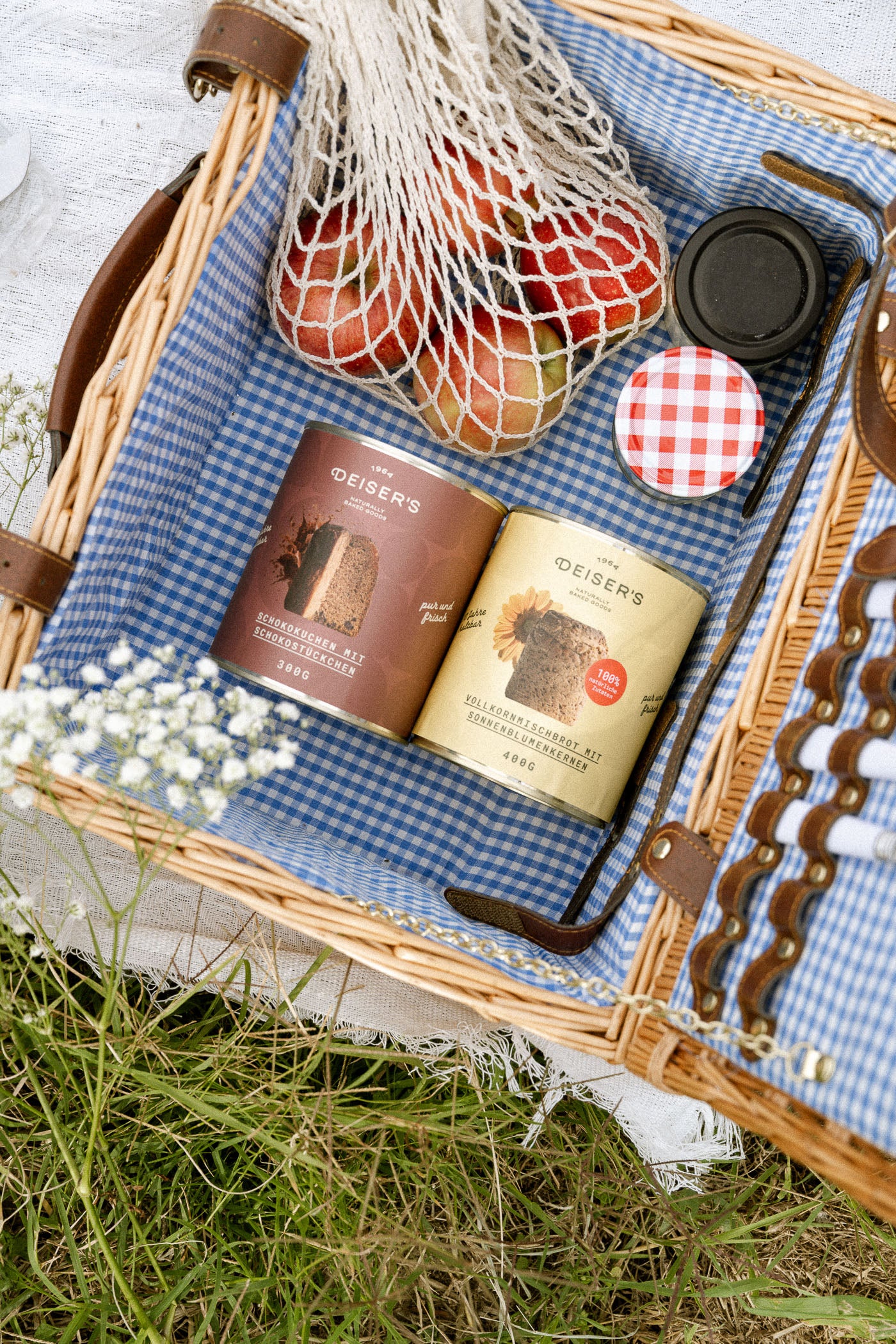 Der Blick in einen Picknickkorb, in dem eine Dose Deiser's Original Schokokuchen und eine Dose Deiser's Original Sonnenblumenbrot liegen, rundherum weitere Leckereien.