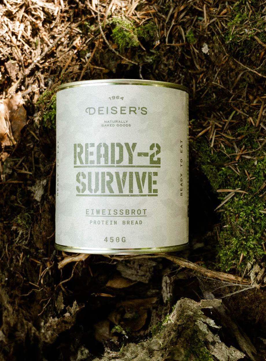Eine Dose Ready-2-Survive Eiweißbrot liegt auf einem Waldboden mit Moos. 