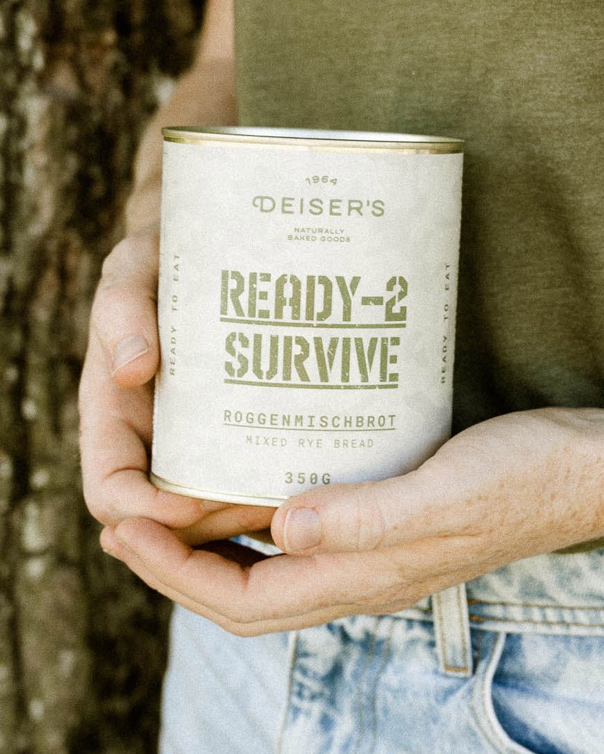 Zwei Hände halten eine Dose Ready-2-Survive Roggenmischbrot. Im Hintergrund sieht man eine Jeans und ein grünes T-Shirt. Die Hände haben Sommersprossen. 